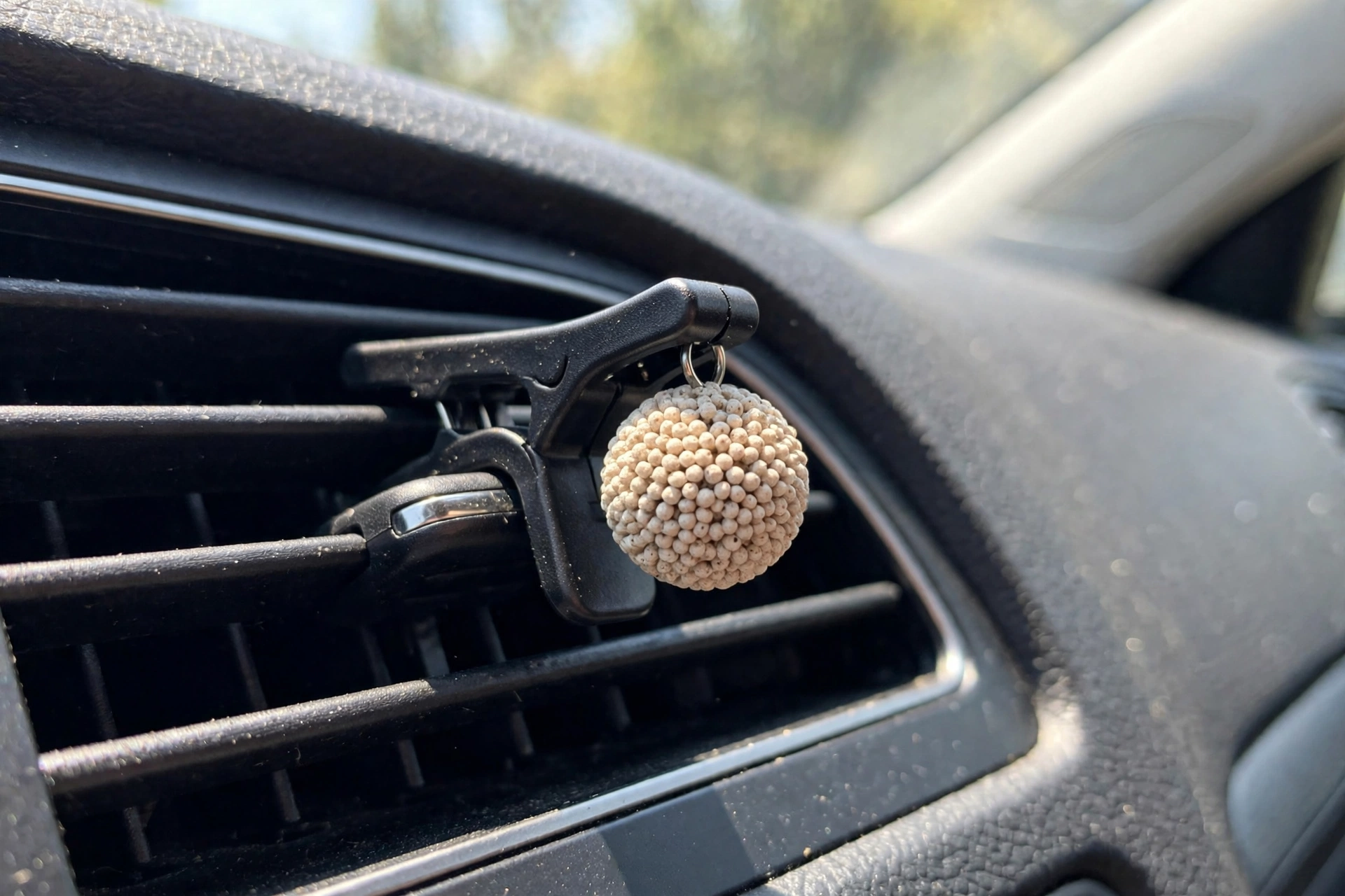 Small round freshie attached to a vent clip, close-up on a car dashboard vent